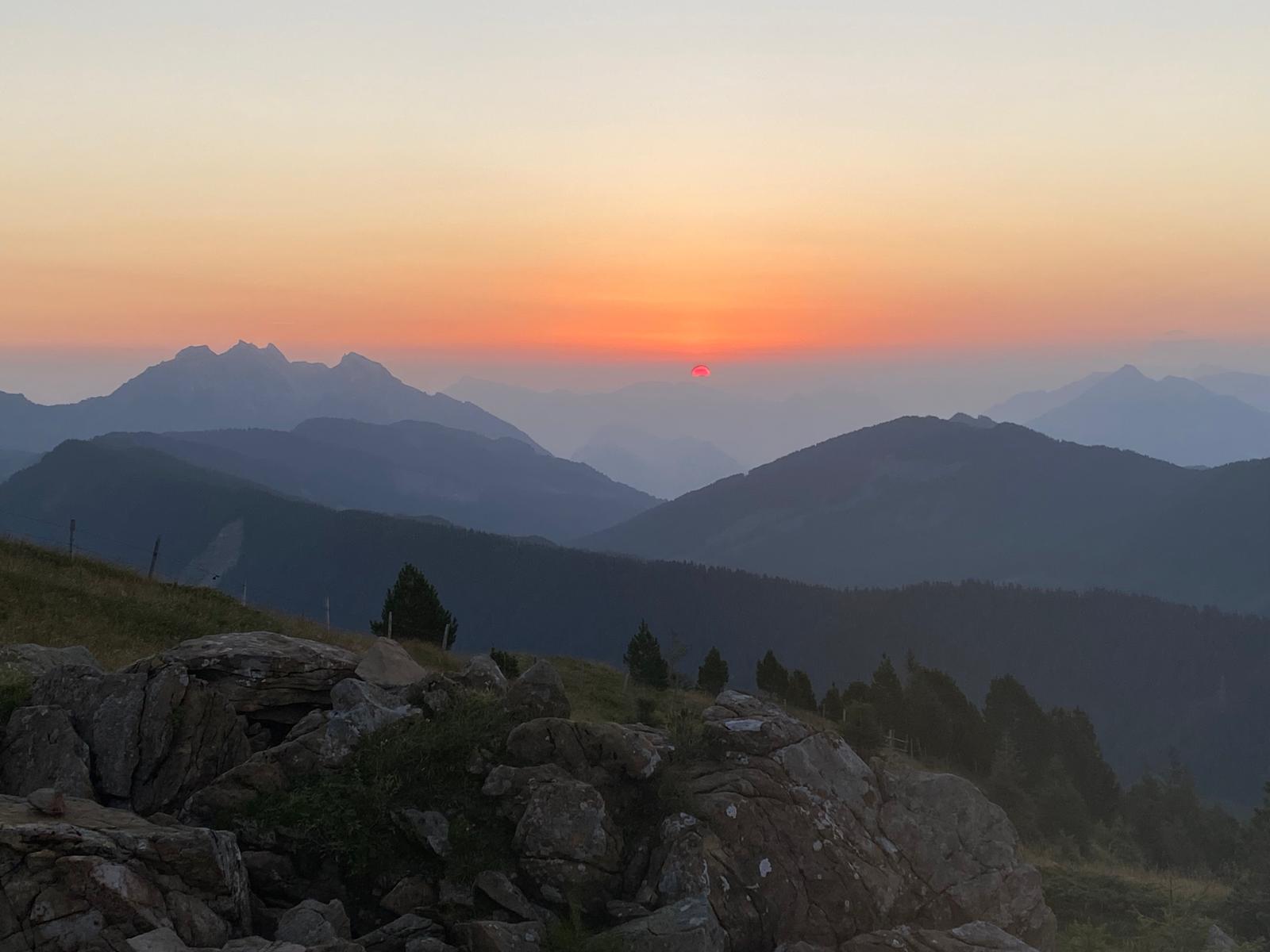 Roter Sonnenhalbkreis über den Bergkuppen, unten blaugrauer und oben rötlich-oranger Himmel beim Sonnenaufgang am Rickhubel